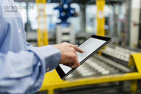 Älterer Geschäftsmann arbeitet in einer Fabrik an einem digitalen Tablet
