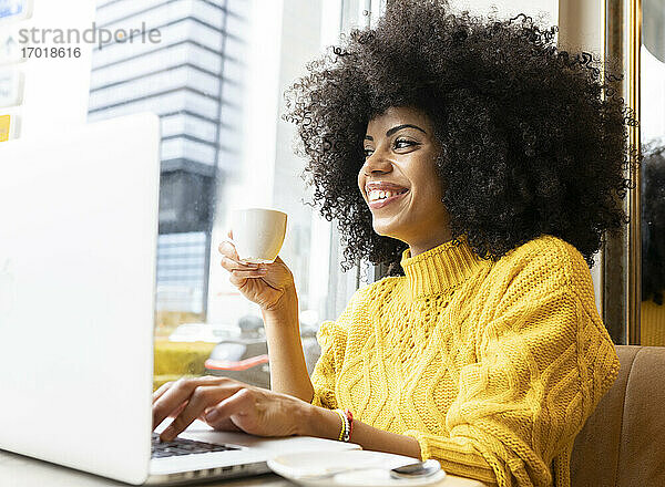 Lächelnde Frau mit Kaffeetasse und Laptop in einem Café sitzend