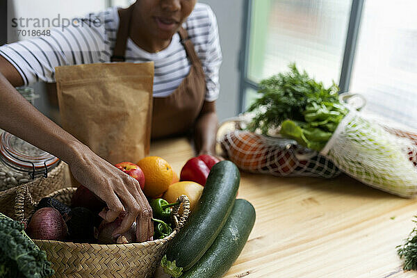 Frau mit Schürze in der Küche  beim Auspacken von frisch gekauftem Bio-Obst und -Gemüse