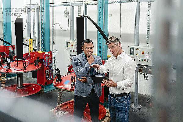 Reife männliche Mitarbeiter  die über ein digitales Tablet in einer Fabrik diskutieren