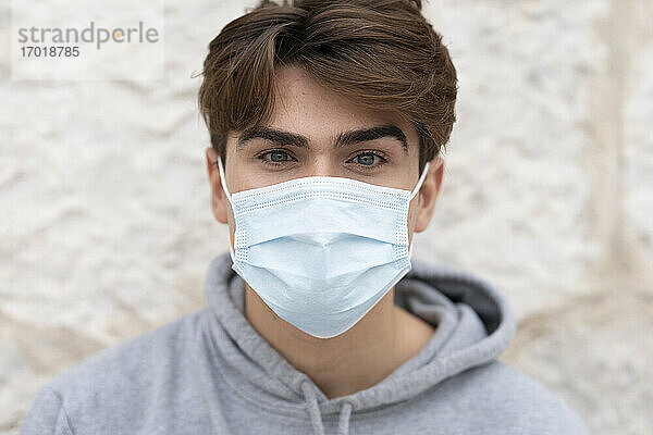 Junger Mann mit Gesichtsschutzmaske an der Wand während des Coronavirus