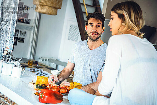 Junger Mann bereitet Essen zu und spricht mit seiner Freundin in der Küche zu Hause