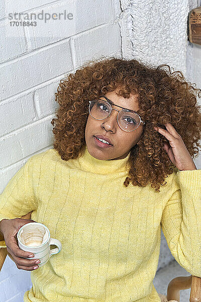 Frau hält Kaffeetasse mit Hand im Haar in einem Café