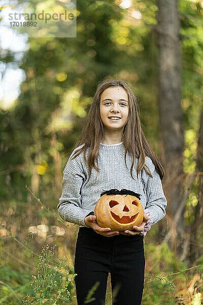 Lächelndes Mädchen  das einen Halloween-Kürbis hält  während es im Park steht