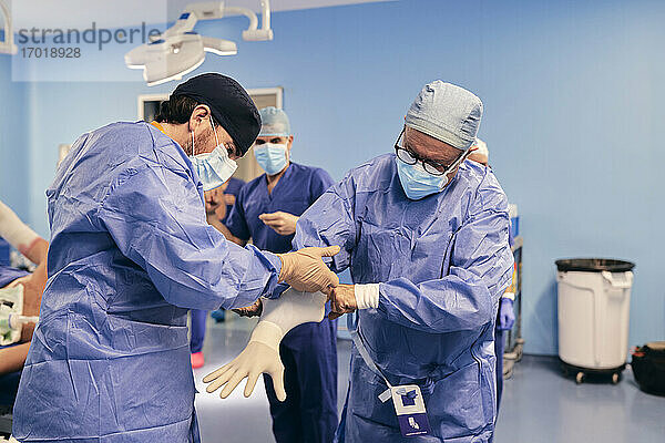 Assistentin  die dem Arzt hilft  einen Schutzhandschuh zu tragen  während er im Operationssaal steht