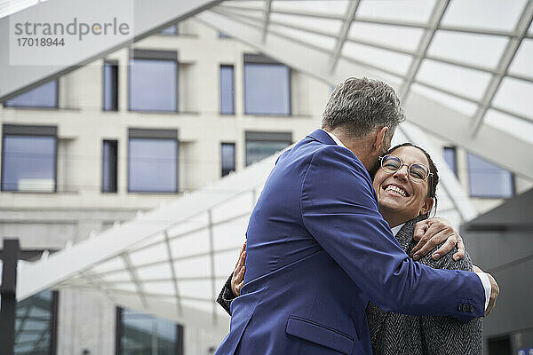 Älterer Geschäftsmann umarmt fröhliche Geschäftsfrau bei der Begrüßung in der Stadt