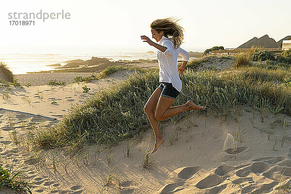 Unbekümmerte Frau  die bei Sonnenuntergang am Strand in den Sand springt