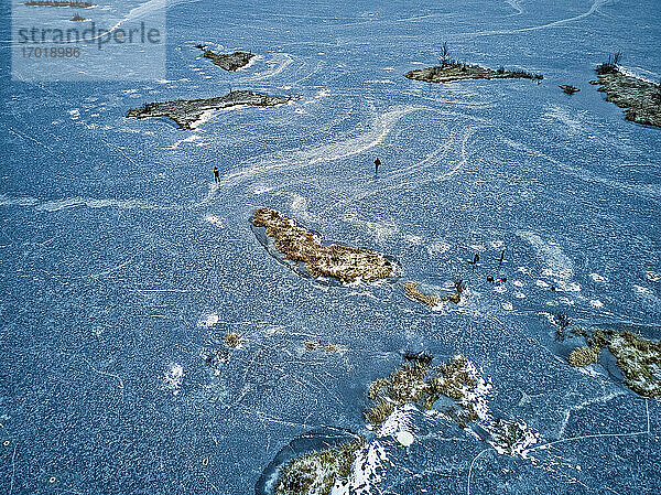 Luftaufnahme von zwei Fischern  die auf der Oberfläche eines zugefrorenen Sees spazieren gehen