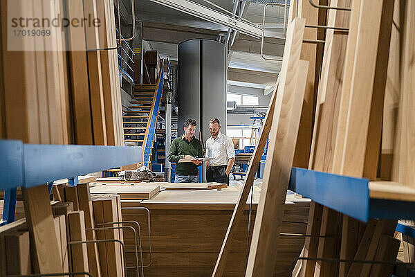 Zwei Zimmerleute unterhalten sich in einer Produktionshalle mit Holzbrettern im Vordergrund