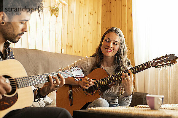 Lächelnde Frau spielt Gitarre und sitzt neben einem Mann zu Hause