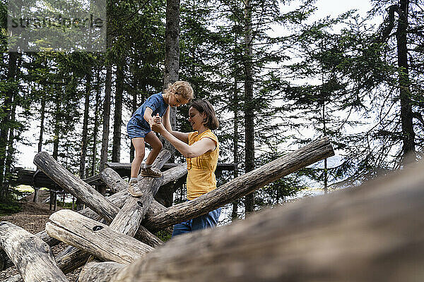 Mutter  die ihrer kleinen Tochter beim Gehen auf einem Holzstamm hilft