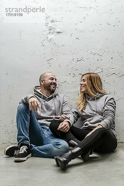 Glückliches Paar im Gespräch auf dem Fußweg vor einer weißen Wand sitzend
