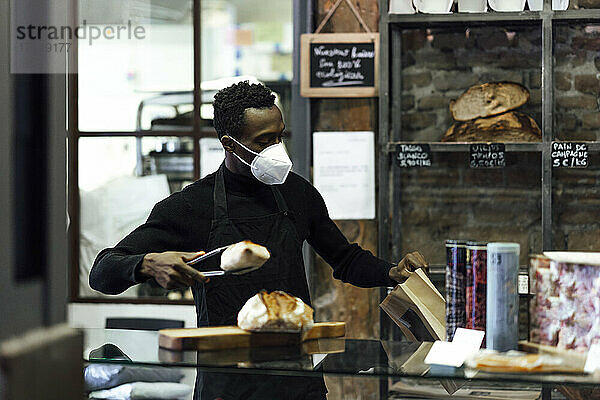 Verkäufer mit Gesichtsmaske beim Verpacken von Brot in einer Bäckerei