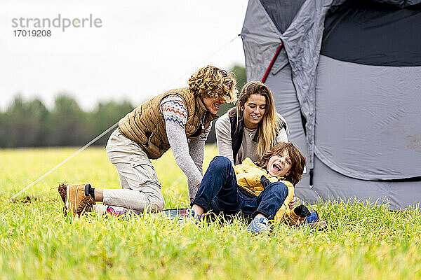 Drei Geschwister spielen im Gras vor einem aufgestellten Zelt