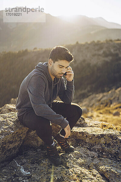 Junger Mann spricht über sein Smartphone  während er auf einem Berg sitzt
