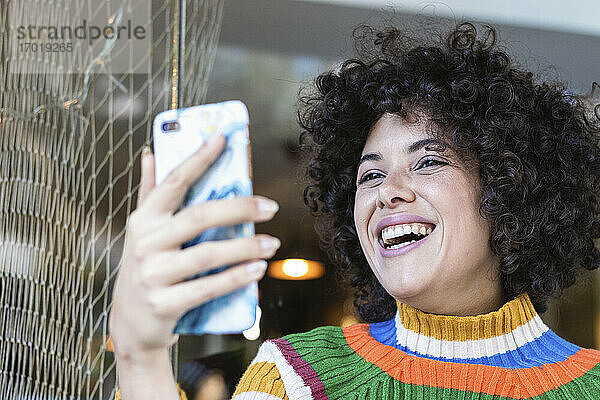 Junge Frau lächelt  während sie im Restaurant ein Mobiltelefon benutzt