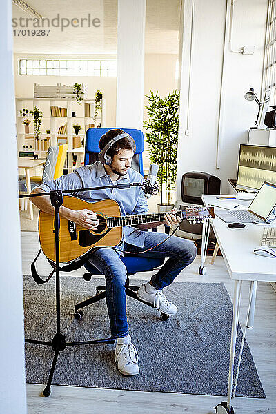 Musiker mit Mikrofon  der Gitarre spielt  während er im Aufnahmestudio sitzt