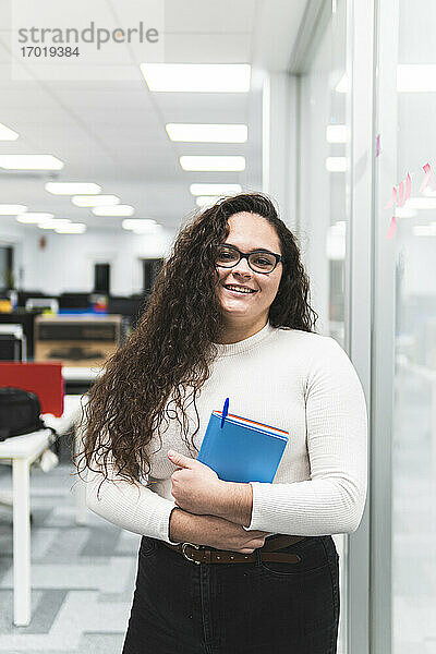 Lächelnde Geschäftsfrau mit Tagebuch auf dem Flur eines Büros