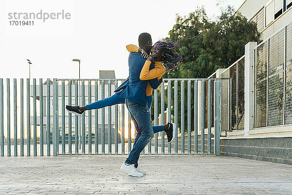 Junger Freund hebt Freundin beim Tanzen auf der Straße hoch