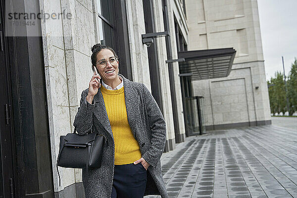 Lächelnde Geschäftsfrau  die mit ihrem Handy telefoniert  während sie in der Stadt spazieren geht