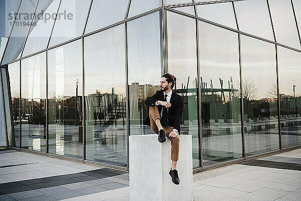 Unternehmer schaut weg  während er an einem Gebäude sitzt
