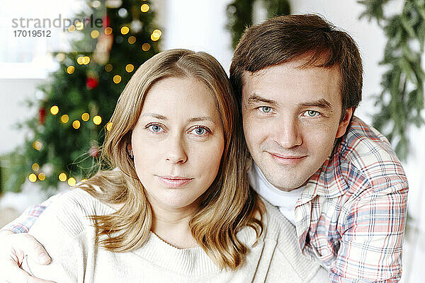 Nahaufnahme eines lächelnden Paares mit Weihnachtsbaum im Hintergrund zu Hause