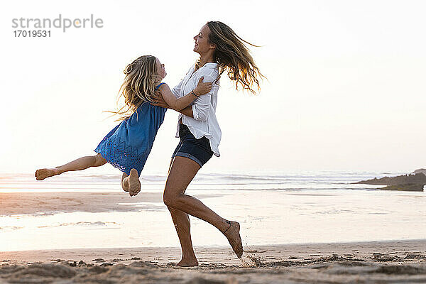 Mutter trägt Tochter beim Spielen am Strand