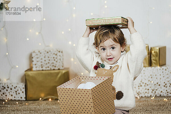 Niedliches kleines Mädchen  das zu Hause sitzend ein Weihnachtsgeschenk öffnet