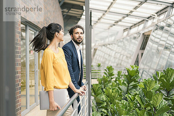 Männliche und weibliche Kollegen lehnen an einem Geländer im Büroflur
