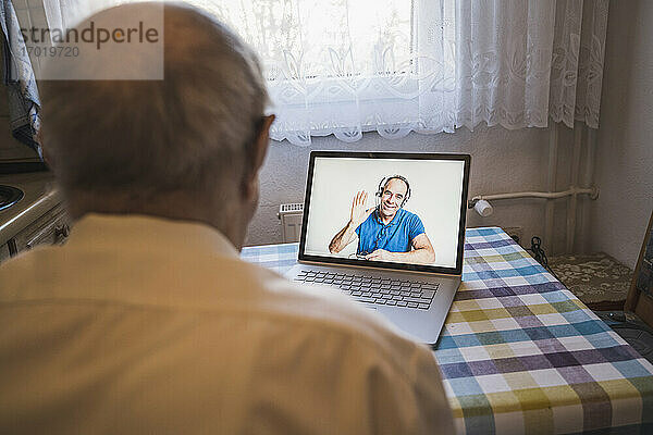 Reifer Mann grüßt älteren Mann per Videoanruf über Laptop zu Hause