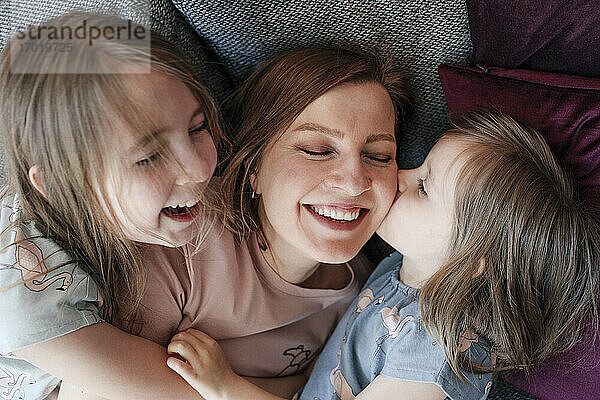 Glückliche Töchter  die ihre Mutter umarmen  während sie sich zu Hause auf die Couch legen