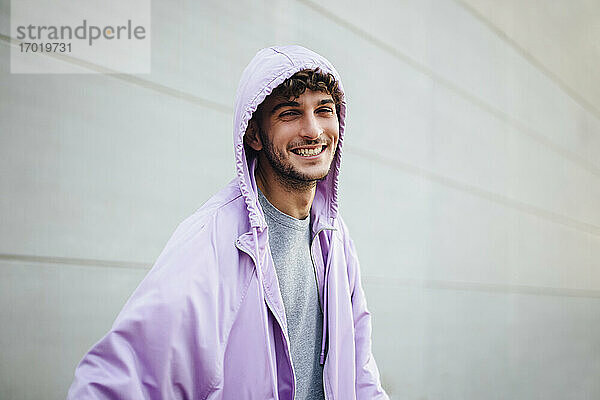 Lächelnder Mann in violetter Jacke vor grauer Wand