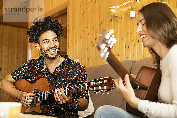 Lächelndes Paar spielt Gitarre  während es zu Hause sitzt