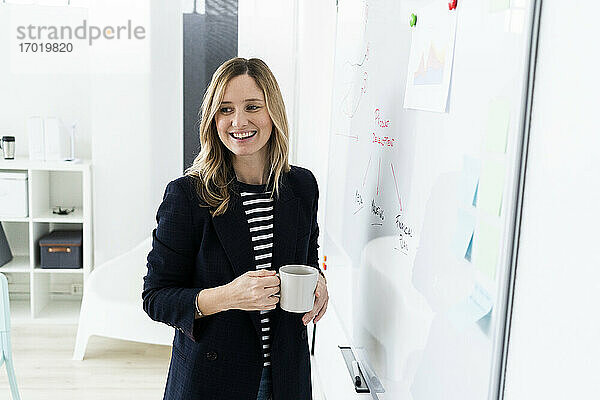 Lächelnde Geschäftsfrau am Whiteboard im Büro stehend