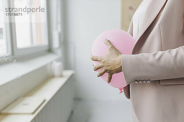 Geschäftsfrau hält Luftballon vor dem Bauch im Büro