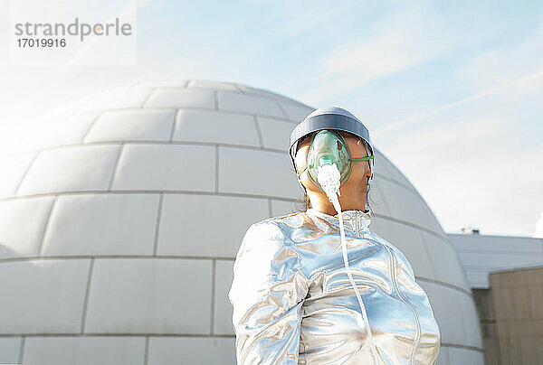 Forscher im glänzenden Raumanzug mit futuristischer Sonnenbrille und Sauerstoffmaske  der wegschaut  während er vor einem Iglu steht