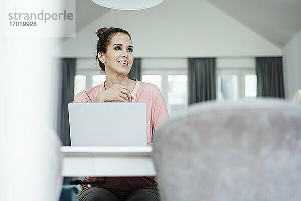 Glückliche reife Geschäftsfrau mit Laptop  die im Büro zu Hause sitzt und träumt