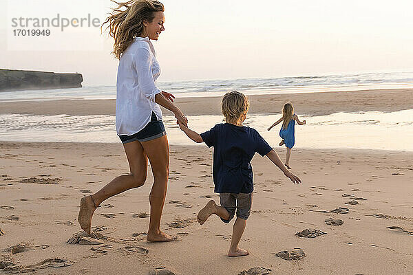 Fröhliche Mutter läuft beim Spielen mit Kindern am Strand