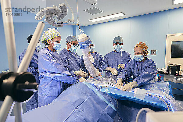 Ärzte mit Gesichtsmaske bei der arthroskopischen Operation eines Patienten  während sie im Operationssaal bei COVID-19 am Tisch stehen