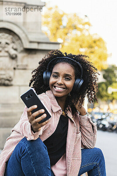 Lächelnde modische junge Frau nimmt Selfie beim Hören von Musik in der Stadt