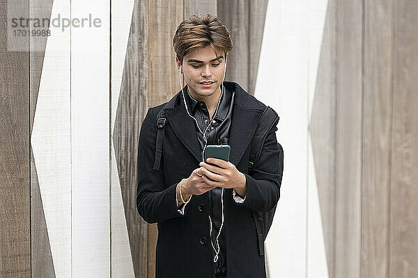 Gut aussehender junger Mann  der sein Smartphone an der Wand benutzt