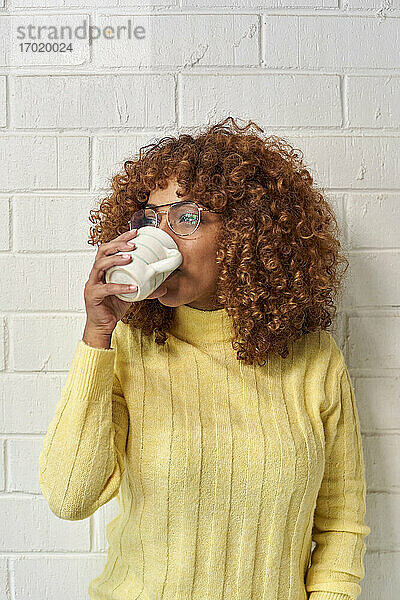 Frau trinkt Kaffee und schaut weg gegen eine Mauer
