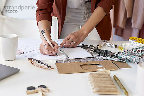 Weibliche Modefachkraft schreibt in persönlichen Organizer am Schreibtisch im Designstudio