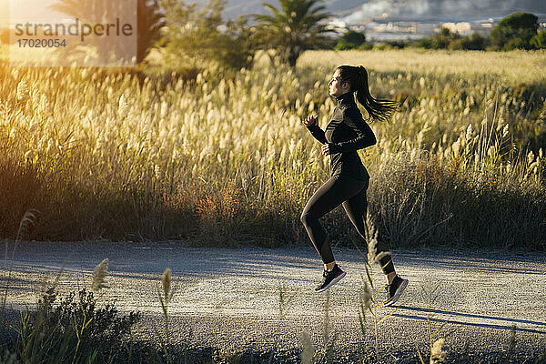 Junge Frau läuft auf dem Fußweg gegen grüne Landschaft bei Sonnenuntergang
