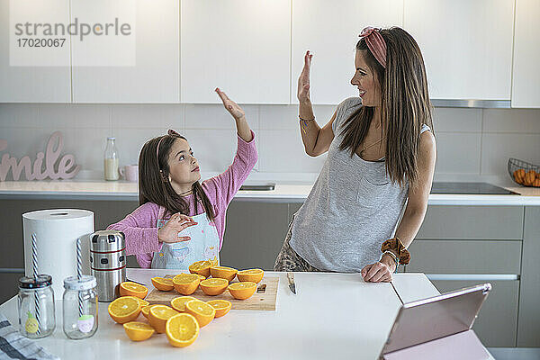Mutter und Tochter geben sich High-Five  während sie in der Küche Orangensaft zubereiten