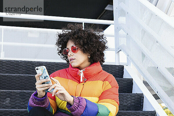 Frau benutzt Mobiltelefon  während sie auf einer Treppe sitzt