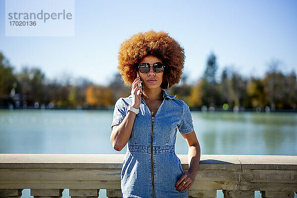 Afrohaarige Frau mit Sonnenbrille telefoniert am Teich Estanque Grande Del Retiro an einem sonnigen Tag  Spanien