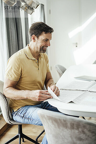 Glücklicher reifer Mann blättert eine Zeitung auf dem Tisch zu Hause um