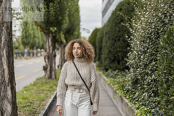 Schöne junge Frau schaut weg  während sie auf dem Fußweg in der Stadt spazieren geht