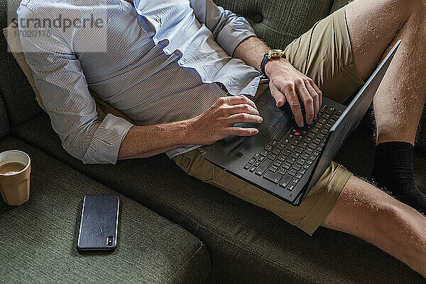 Mann bindet Laptop um  während er zu Hause auf der Couch sitzt